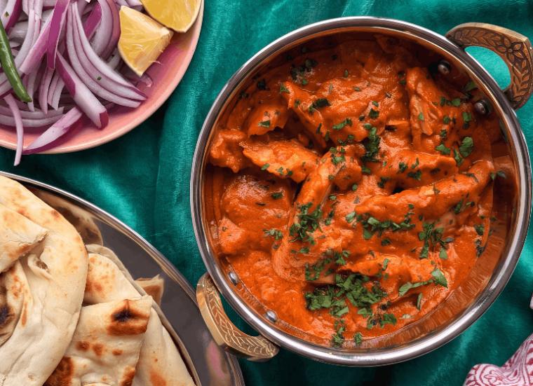 Karahi of butter chicken with naan and sliced onions